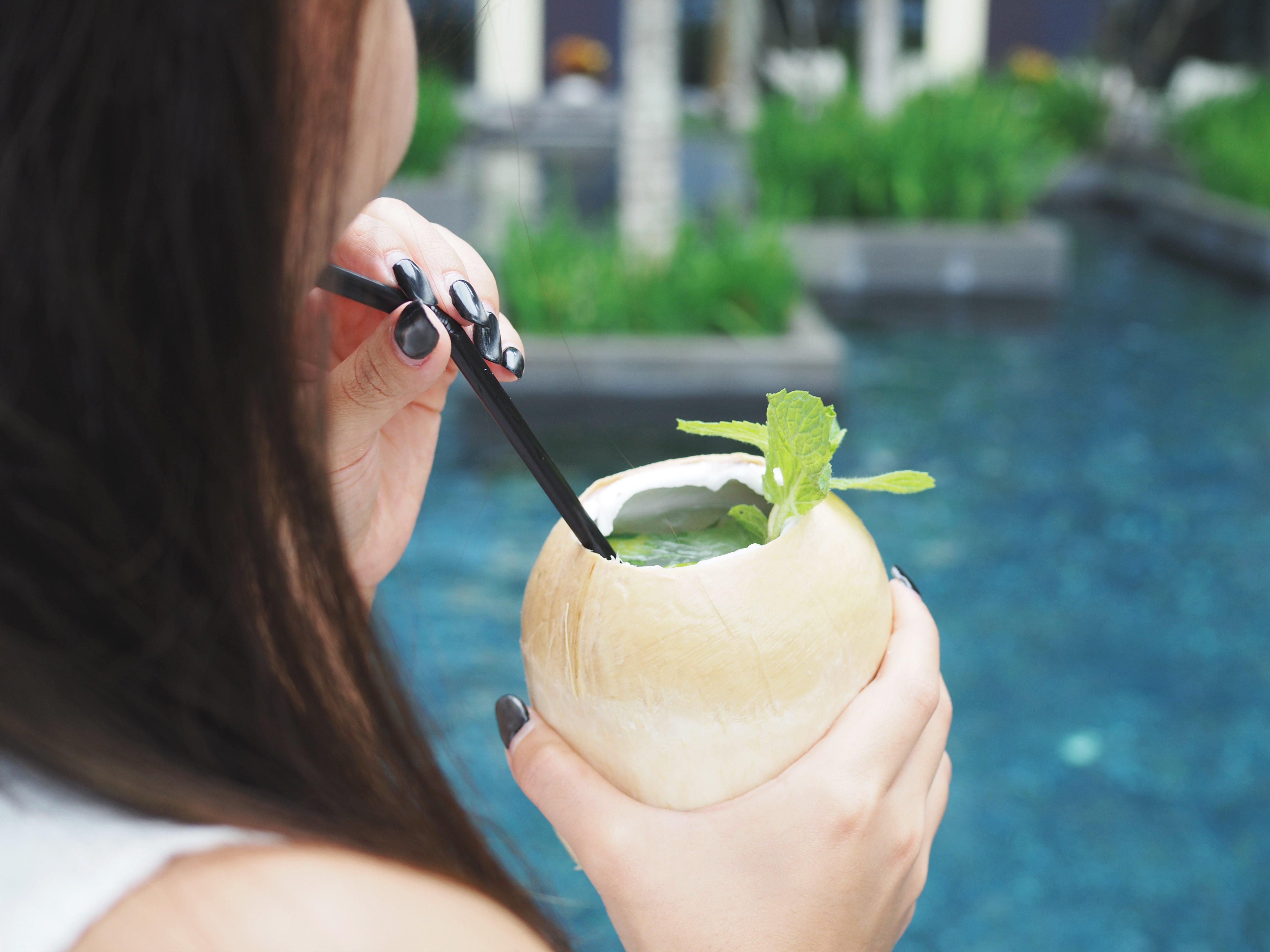 Crowne Plaza Changi Airport By Ihg Σιγκαπούρη Εξωτερικό φωτογραφία The photo features a person holding a coconut drink with a straw. The drink is garnished with a sprig of mint. The background shows a blue pool, suggesting a tropical or relaxing setting. The focus is on the drink and the person's hand.