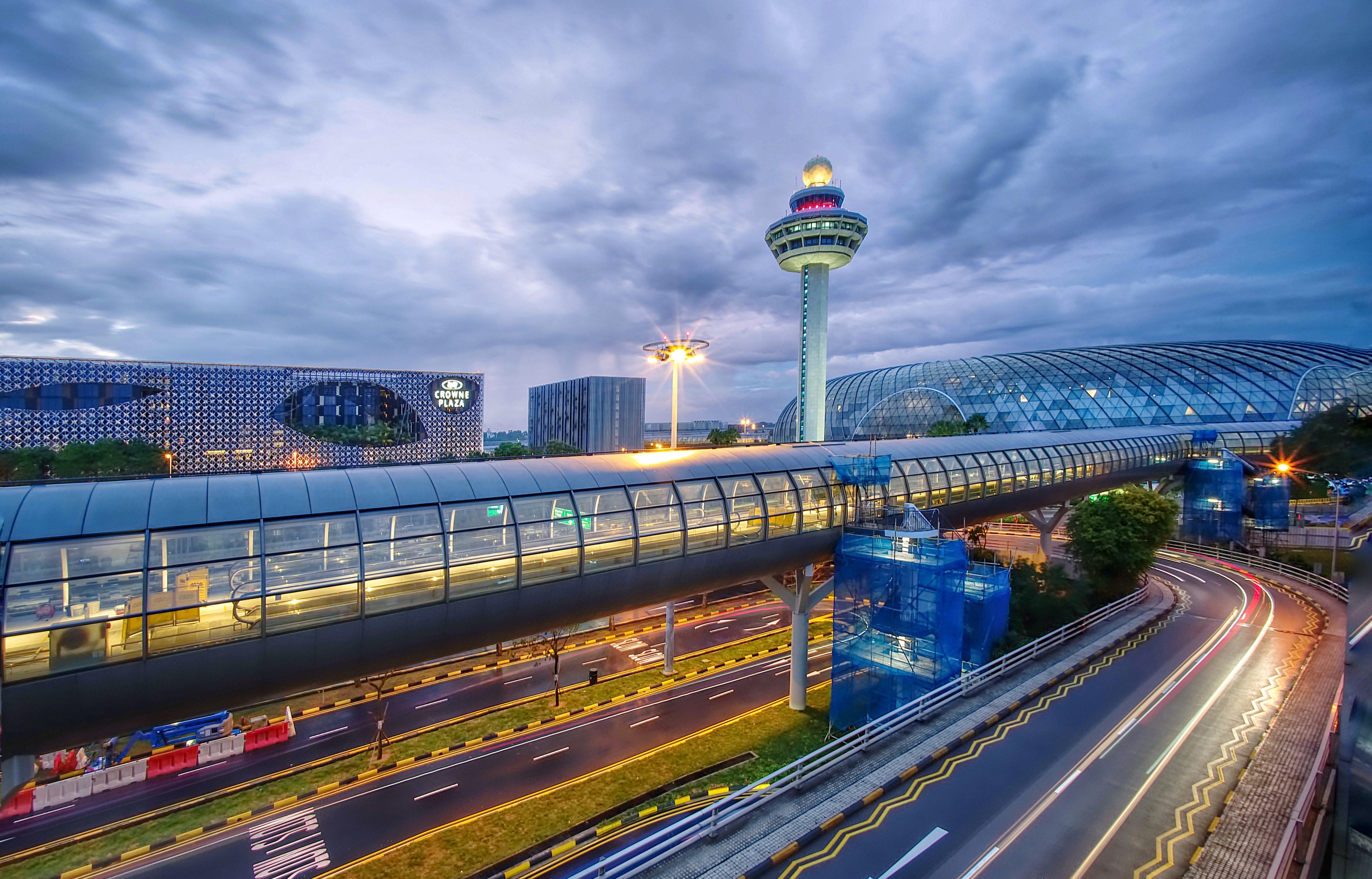 Crowne Plaza Changi Airport By Ihg Σιγκαπούρη Εξωτερικό φωτογραφία The photo depicts an airport scene, likely featuring a modern terminal structure with a distinctive, futuristic design. In the foreground, there is a pedestrian bridge or walkway, along with roads leading to the terminal. A control tower can be seen 