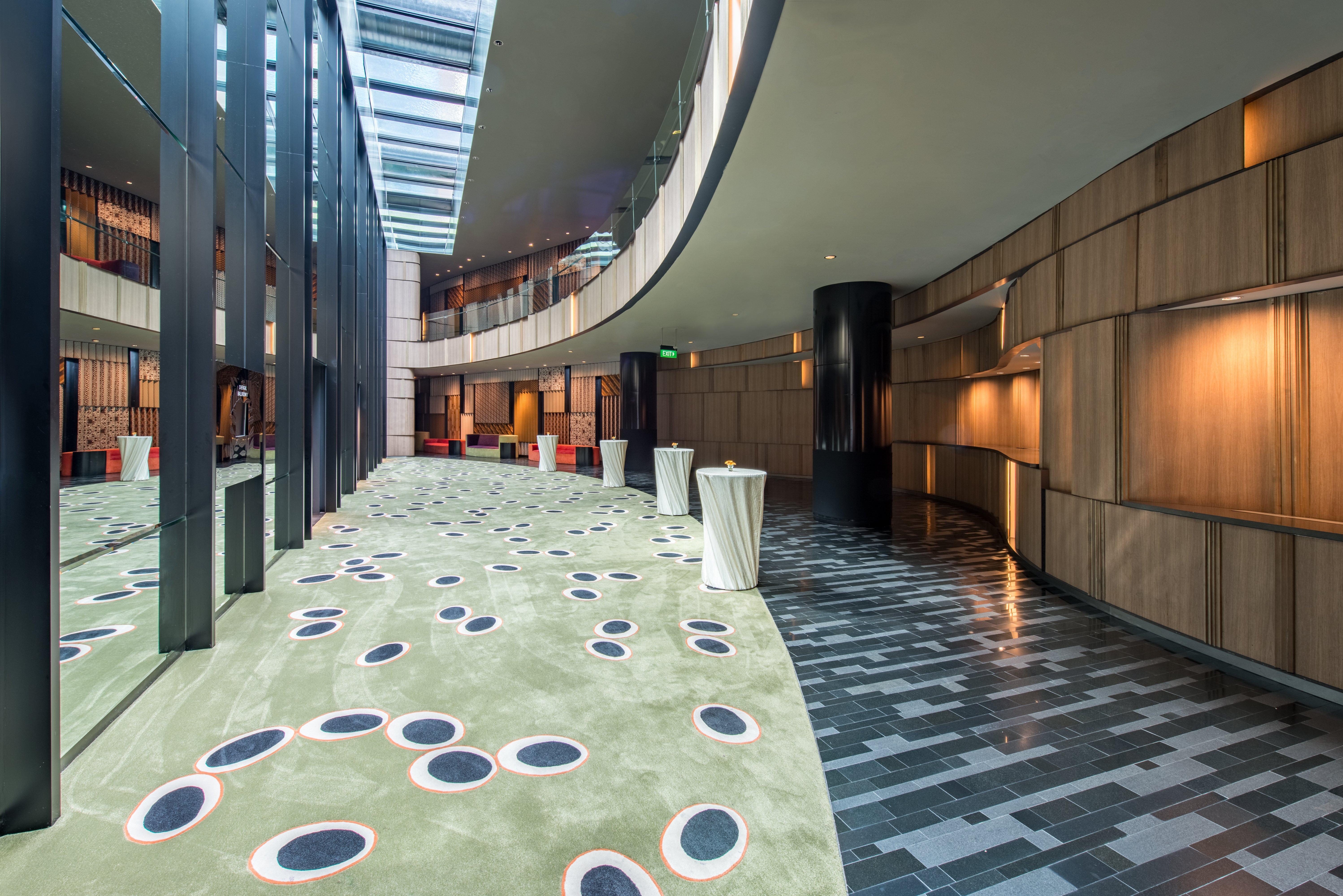 Crowne Plaza Changi Airport By Ihg Σιγκαπούρη Εξωτερικό φωτογραφία The photo shows a modern indoor space that features a curved hallway with a mix of materials and textures. The floor is divided into two sections: one has a smooth, dark tiled design, while the other has a soft, green carpet with circular patterns in