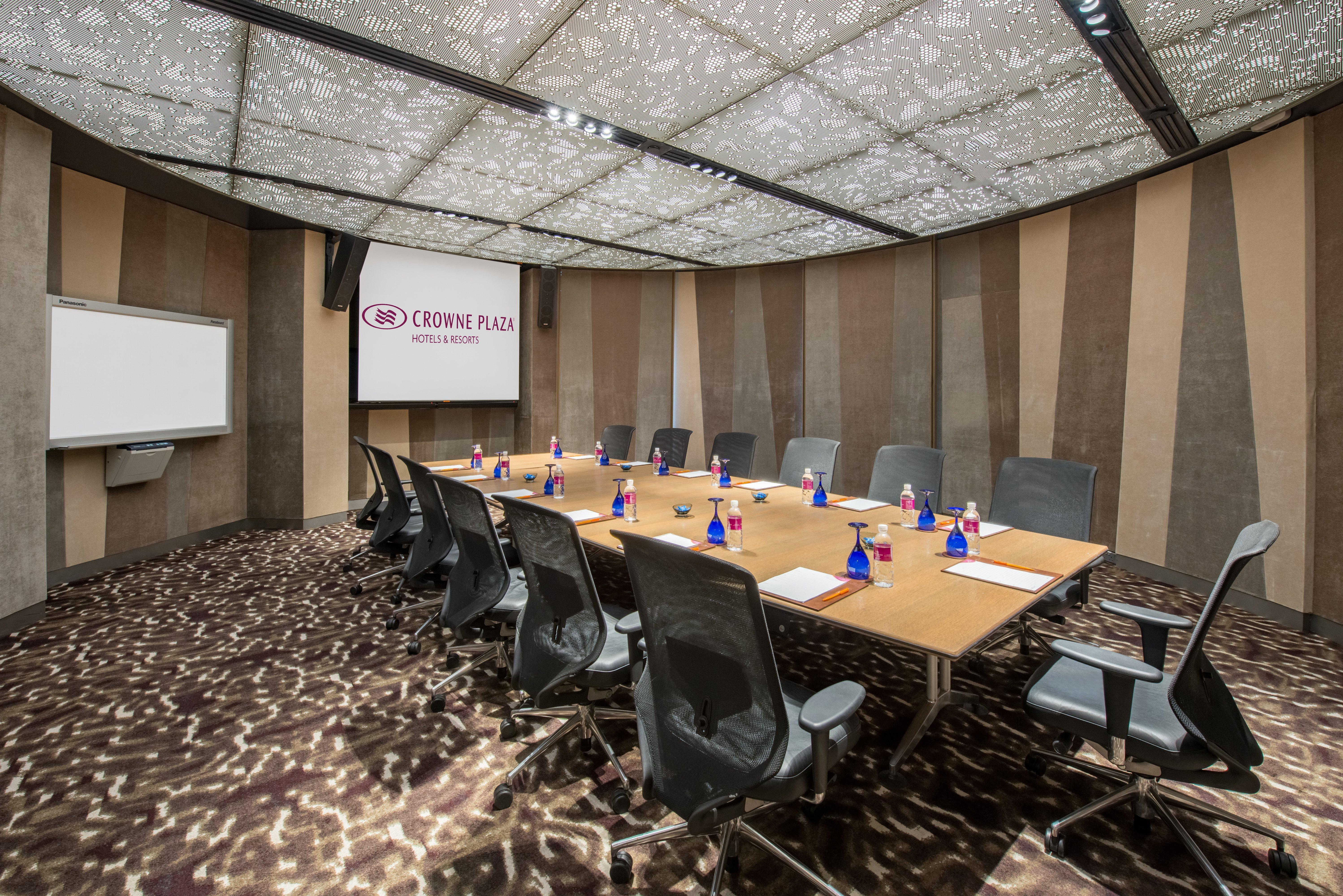 Crowne Plaza Changi Airport By Ihg Σιγκαπούρη Εξωτερικό φωτογραφία The photo shows a modern conference room. It features a large, rectangular wooden table surrounded by ergonomic black office chairs. On the table, there are small blue vases, each containing flowers. The room has a unique, patterned ceiling that enha