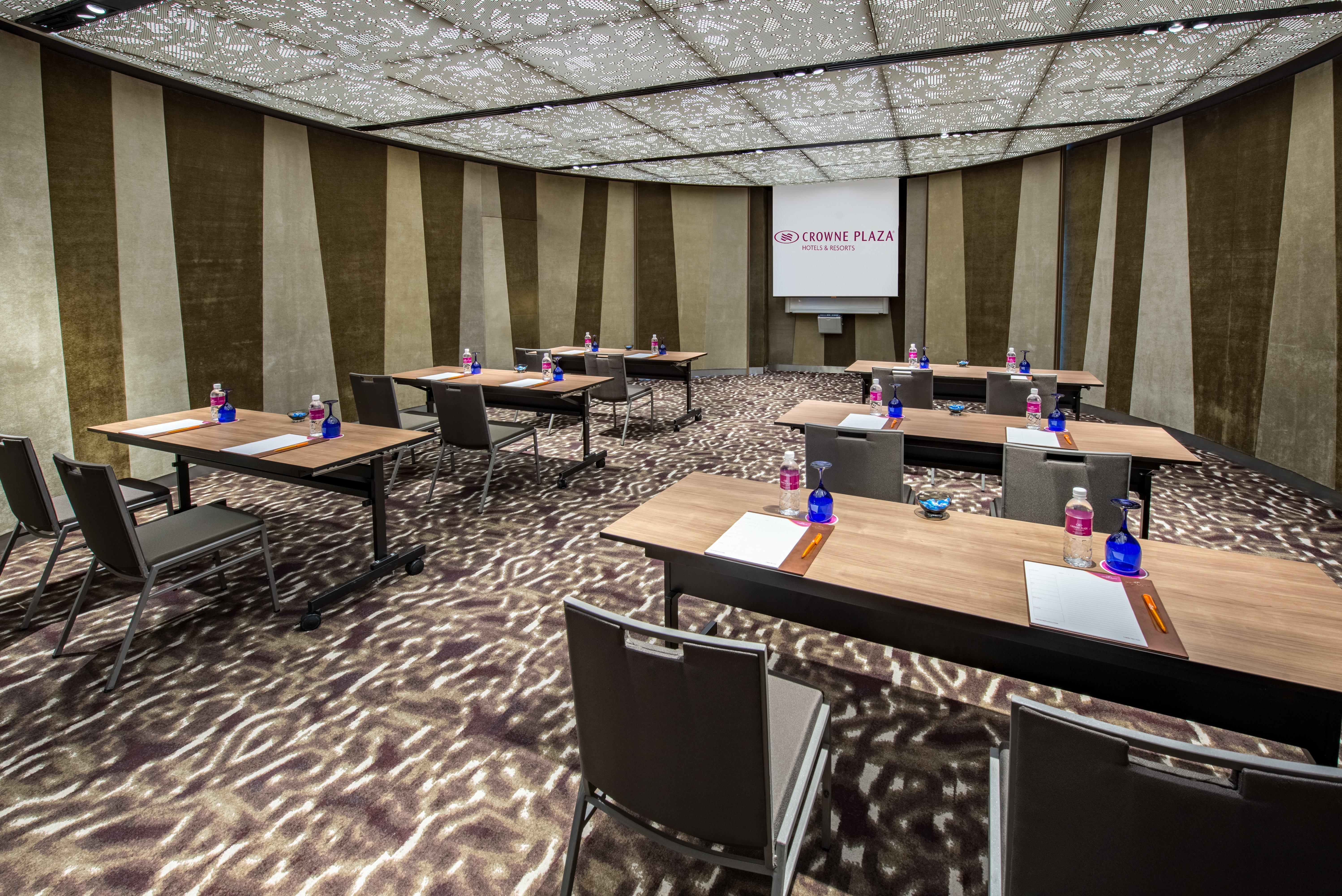 Crowne Plaza Changi Airport By Ihg Σιγκαπούρη Εξωτερικό φωτογραφία The photo shows a modern conference room set up for a meeting or presentation. There are several wooden tables arranged in a U-shape, each equipped with a notepad and pen. Bottled water is placed in blue containers on the tables. The room features a 
