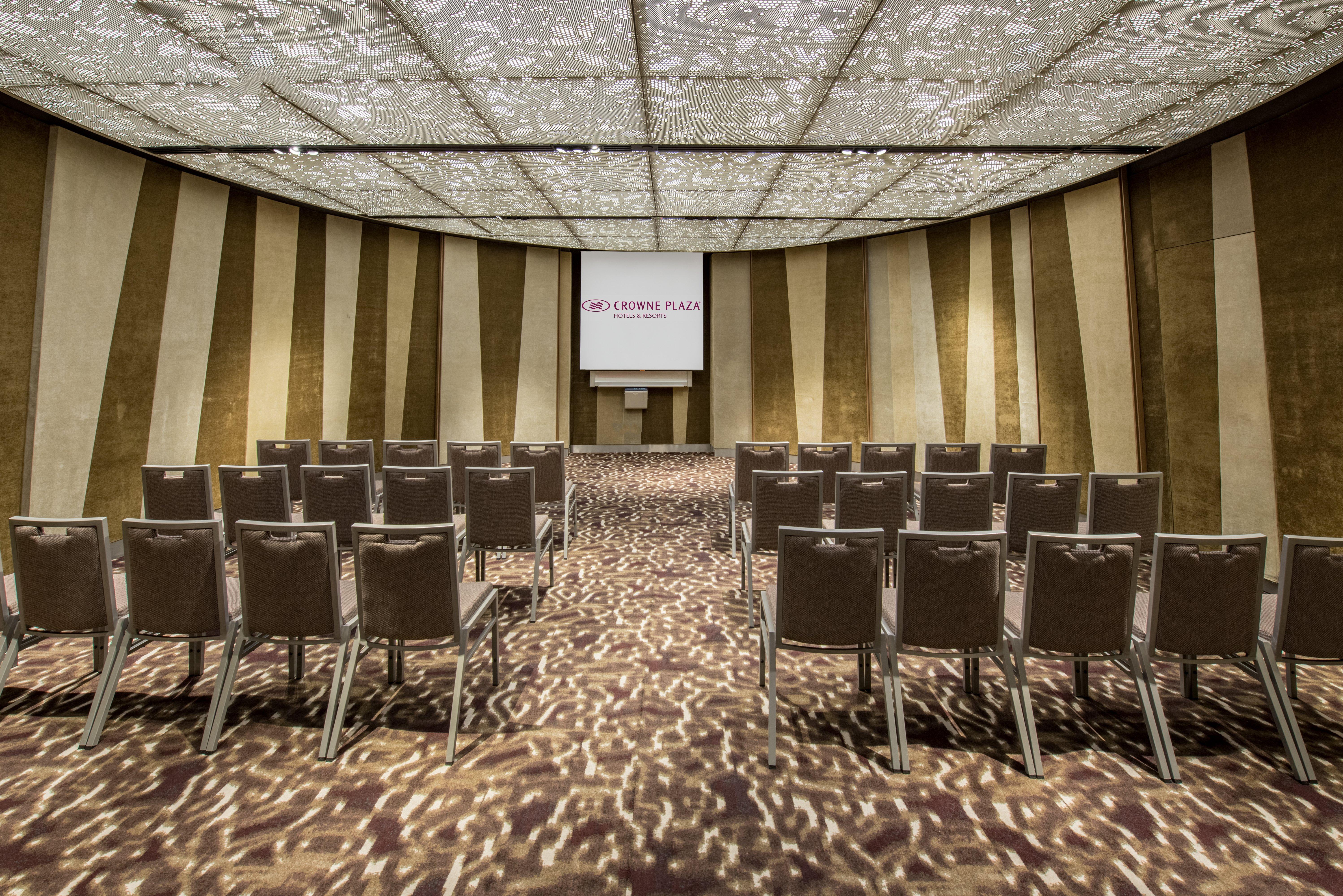 Crowne Plaza Changi Airport By Ihg Σιγκαπούρη Εξωτερικό φωτογραφία The photo shows a conference or meeting room. It features rows of grey chairs arranged in a semi-circular layout, facing a screen at the front. The room has a decorative ceiling with a patterned design that allows light to filter through, creating in