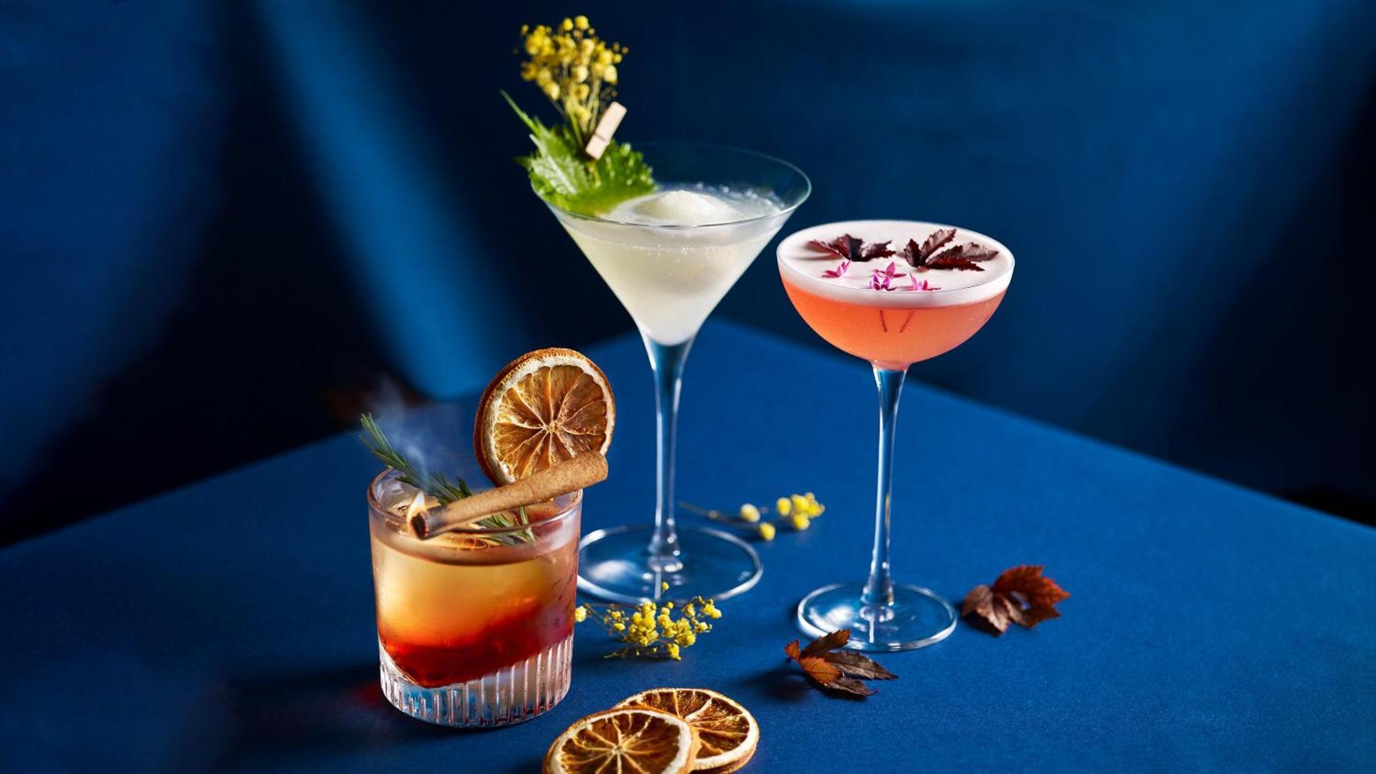 Crowne Plaza Changi Airport By Ihg Σιγκαπούρη Εξωτερικό φωτογραφία The photo shows a stylish arrangement of three cocktails on a blue surface. 

1. **Left Cocktail**: A lowball glass containing a drink with a reddish hue, garnished with a dried orange slice and a cinnamon stick. 

2. **Middle Cocktail**: A classic m