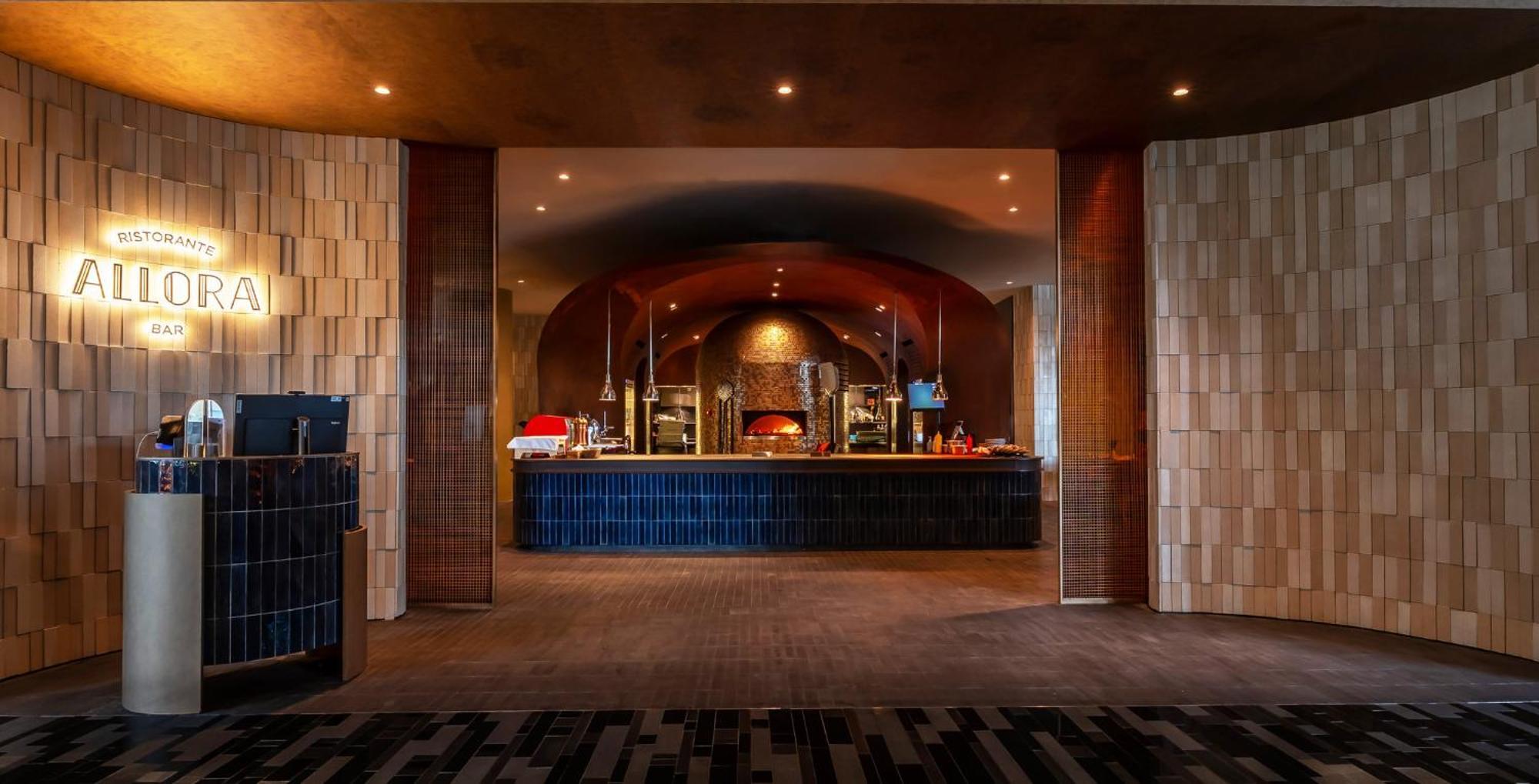 Crowne Plaza Changi Airport By Ihg Σιγκαπούρη Εξωτερικό φωτογραφία The photo shows an interior space that appears to be a restaurant or dining area. In the background, there is a long counter, likely serving food, with an arched design above it. The counter is lined with various food items, possibly in warming trays