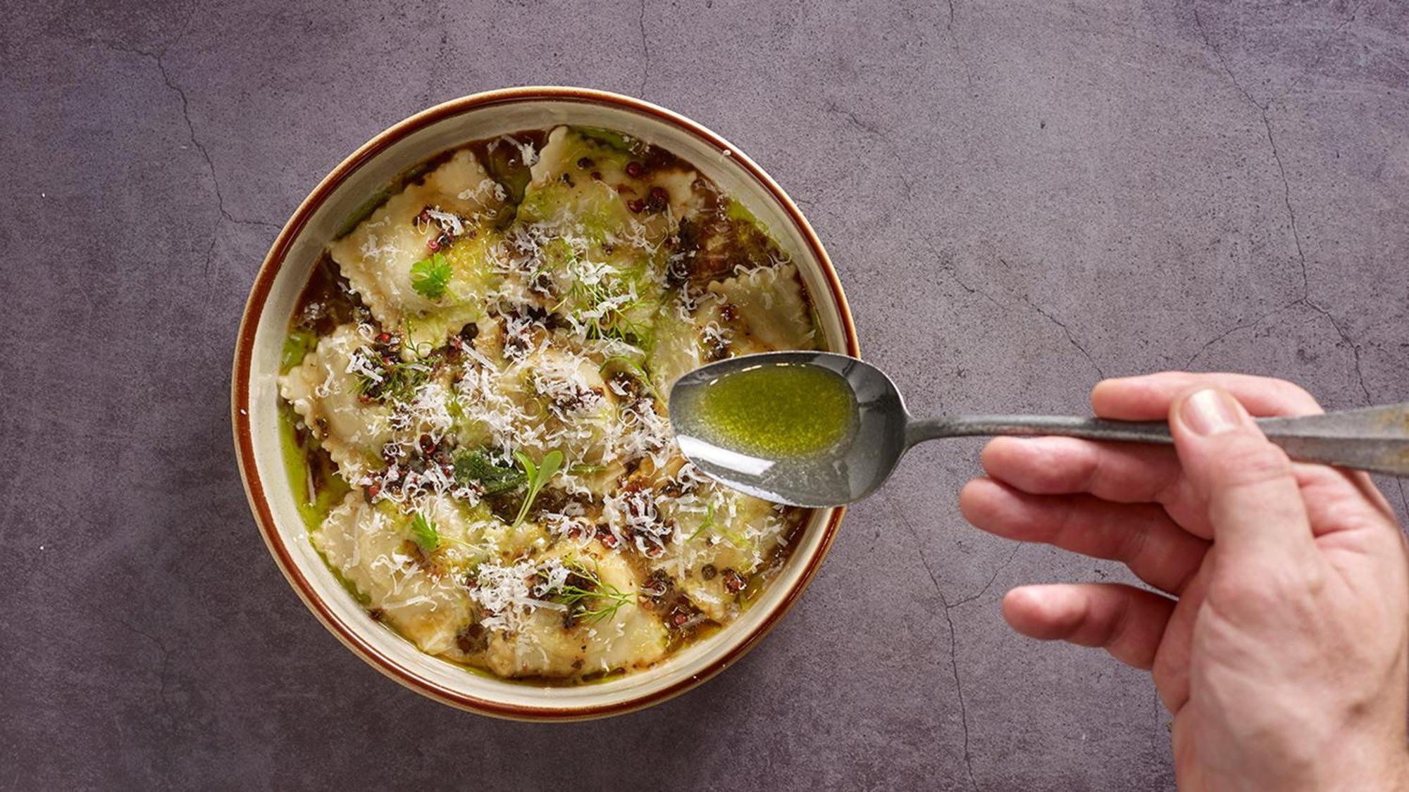 Crowne Plaza Changi Airport By Ihg Σιγκαπούρη Εξωτερικό φωτογραφία The photo shows a bowl of ravioli garnished with grated cheese and drizzled with olive oil. A hand is holding a spoon above the bowl, indicating the action of adding more oil or sauce. The dish appears delicious and is presented with an appealing aes