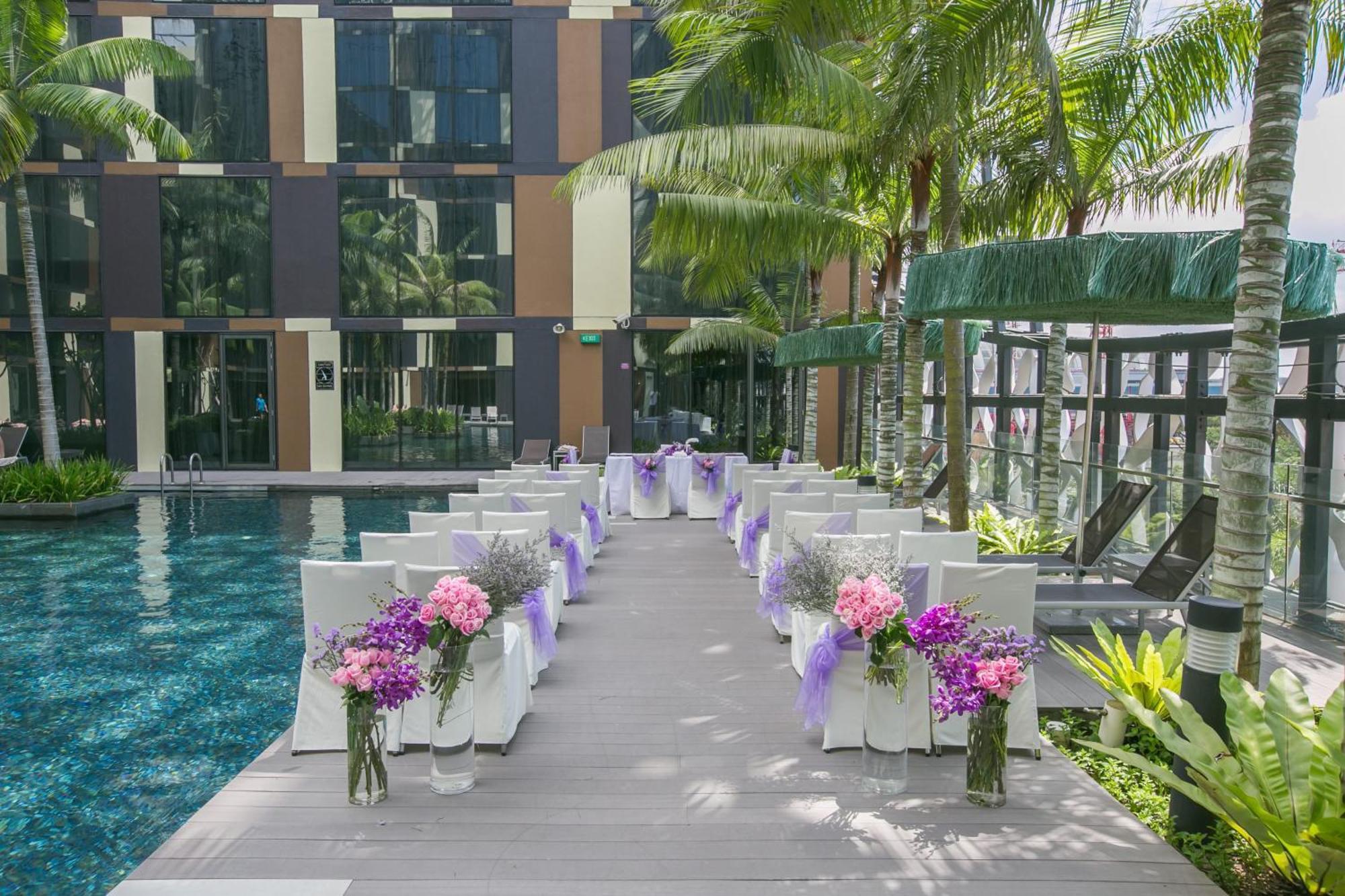Crowne Plaza Changi Airport By Ihg Σιγκαπούρη Εξωτερικό φωτογραφία The photo shows a beautifully arranged outdoor setting for a wedding or a similar event. There is a long aisle made of wooden planks leading to a pool area, flanked by neatly arranged chairs. Each chair is adorned with purple ribbons and decorated wi