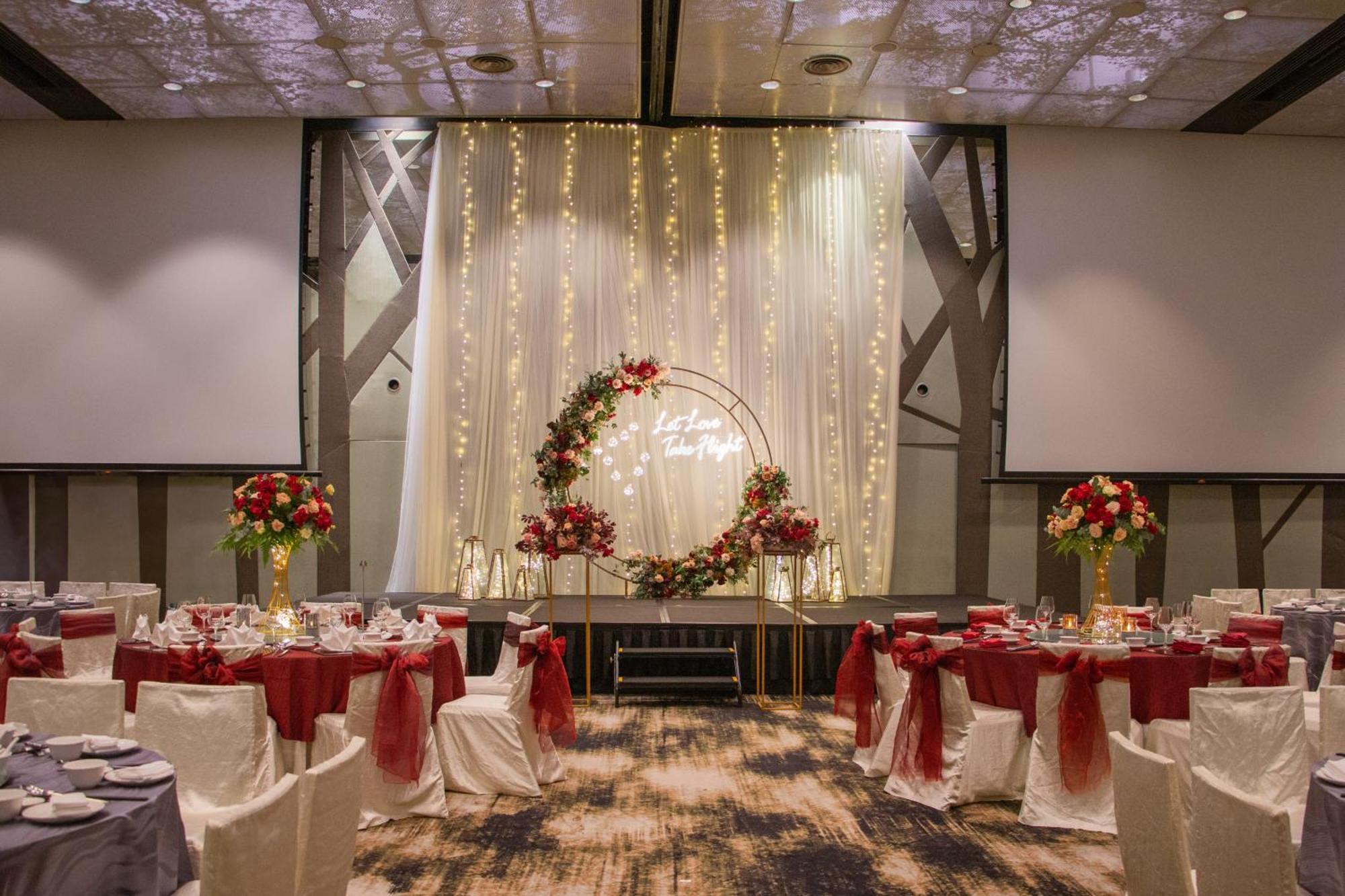 Crowne Plaza Changi Airport By Ihg Σιγκαπούρη Εξωτερικό φωτογραφία The photo shows an elegantly decorated banquet hall set up for an event. There are round tables with white tablecloths, each adorned with a red centerpiece. The chairs have white covers and are draped with red sashes. At the back of the room, there i