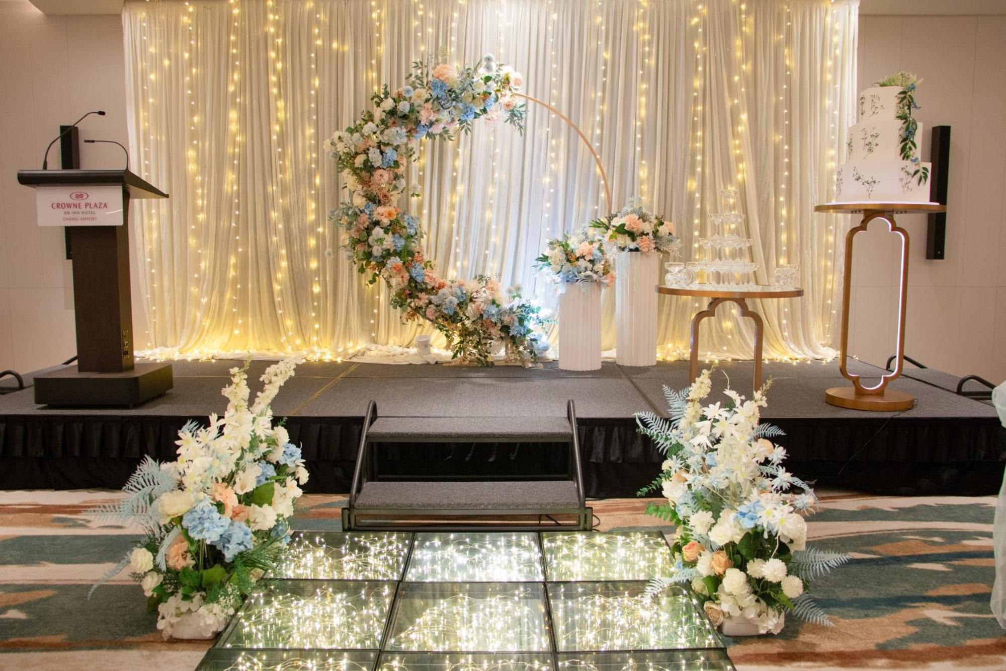 Crowne Plaza Changi Airport By Ihg Σιγκαπούρη Εξωτερικό φωτογραφία The photo shows a beautifully decorated event space, likely for a wedding or special occasion. In the background, there is a shimmering curtain with fairy lights that create a warm, romantic ambiance. 

At the center, there is a circular floral arch 