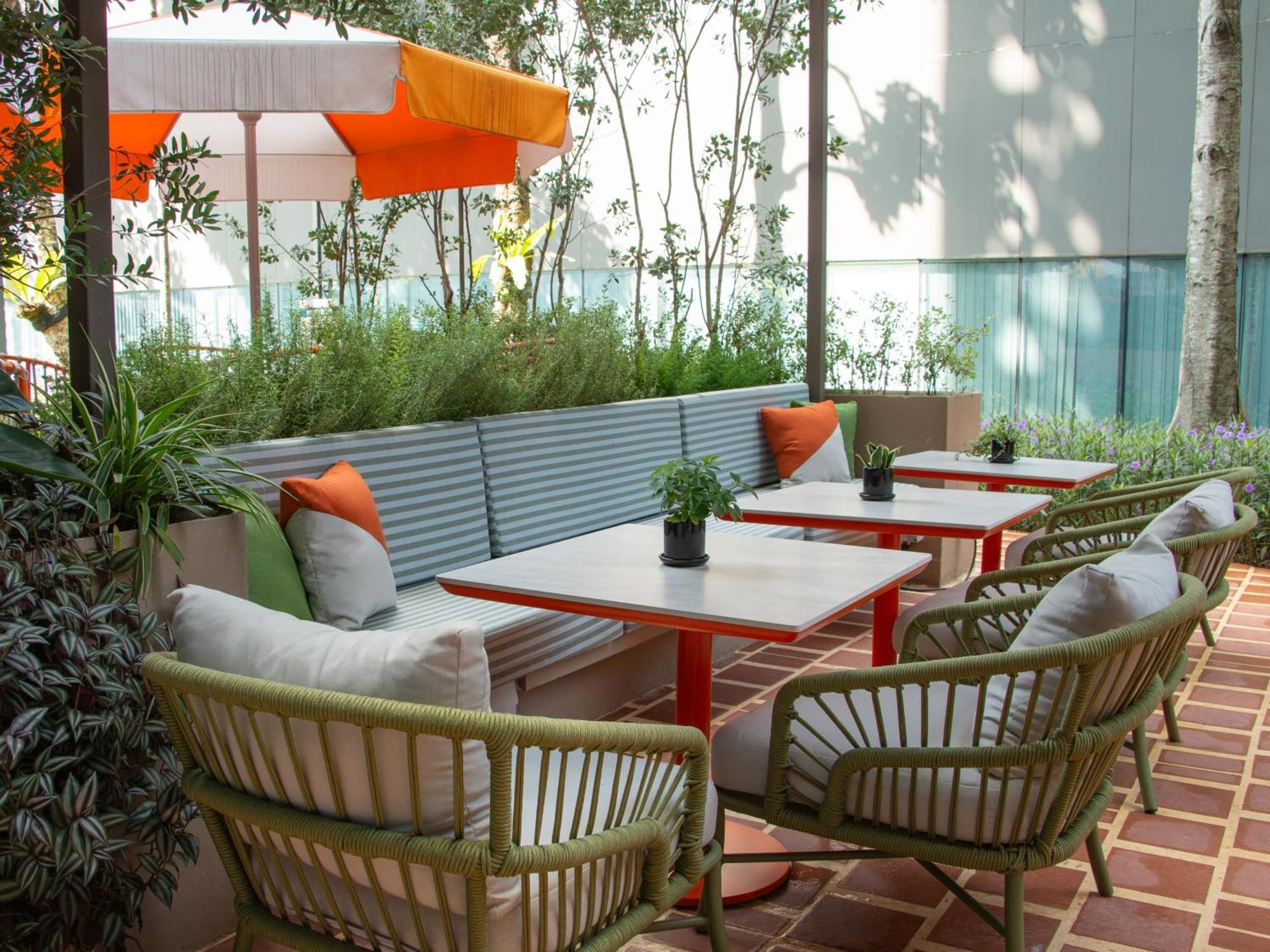 Crowne Plaza Changi Airport By Ihg Σιγκαπούρη Εξωτερικό φωτογραφία The photo shows a cozy outdoor seating area. There are several tables with red metal legs, each accompanied by comfortable chairs. The chairs have a woven design and are in shades of green. There are cushions in various colors on the chairs for added