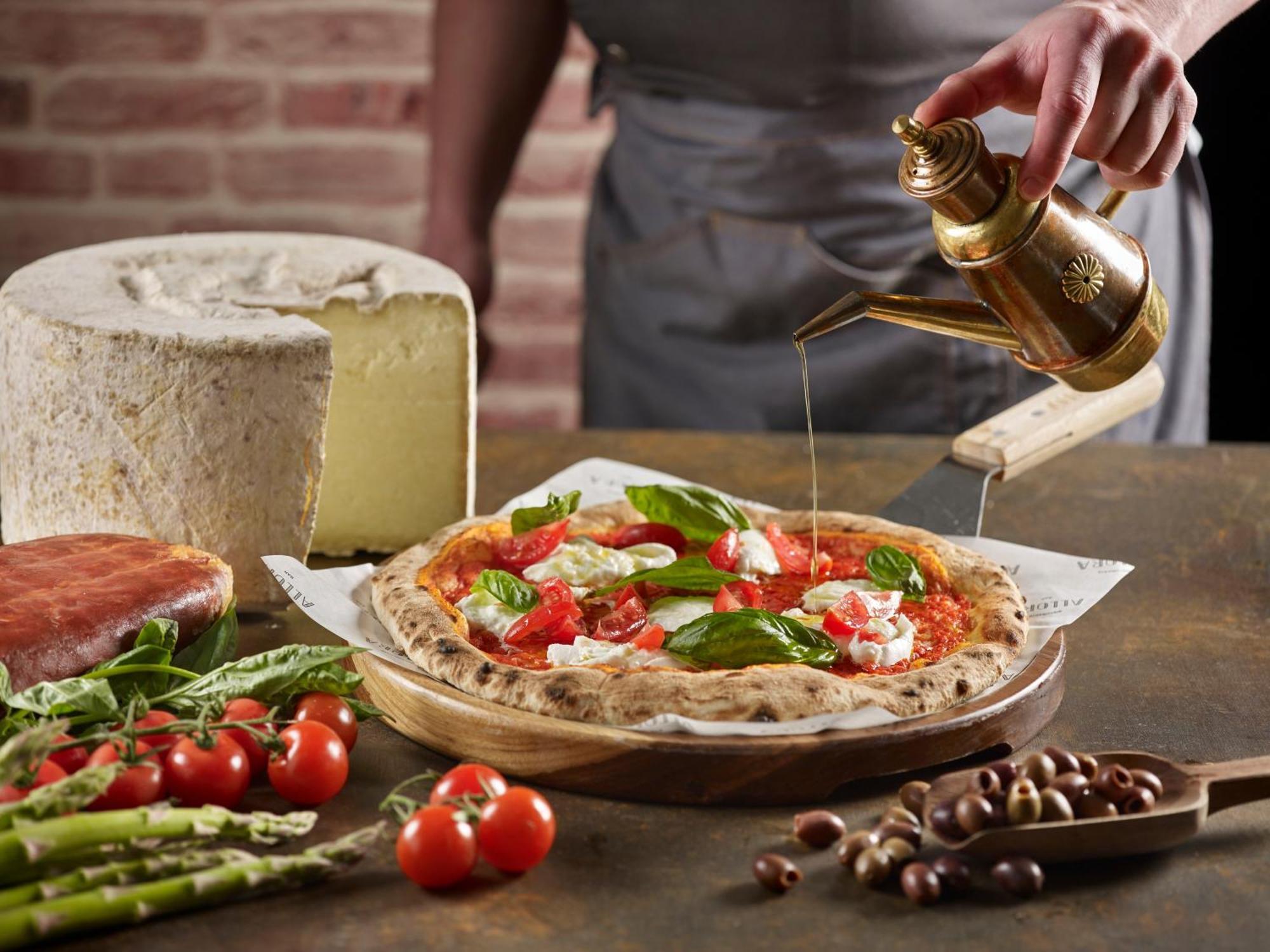 Crowne Plaza Changi Airport By Ihg Σιγκαπούρη Εξωτερικό φωτογραφία The photo features a freshly made pizza being drizzled with oil. The pizza is topped with ingredients such as fresh basil and tomatoes, and has a golden, crispy crust. In the background, there is a block of cheese and a piece of ham. Surrounding the 