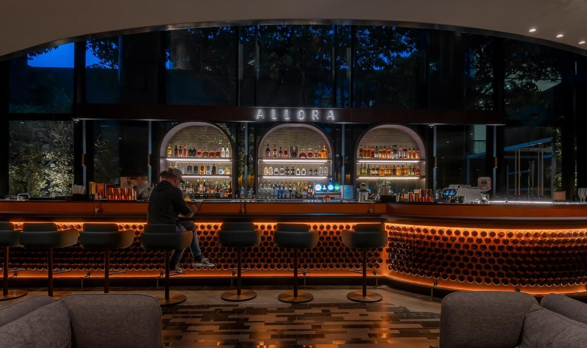 Crowne Plaza Changi Airport By Ihg Σιγκαπούρη Εξωτερικό φωτογραφία The photo shows a bar area with a modern and stylish design. In the center, there is a well-lit bar counter featuring a variety of alcoholic beverages displayed on shelves behind it. The bar has a sleek, contemporary look with circular light fixtures