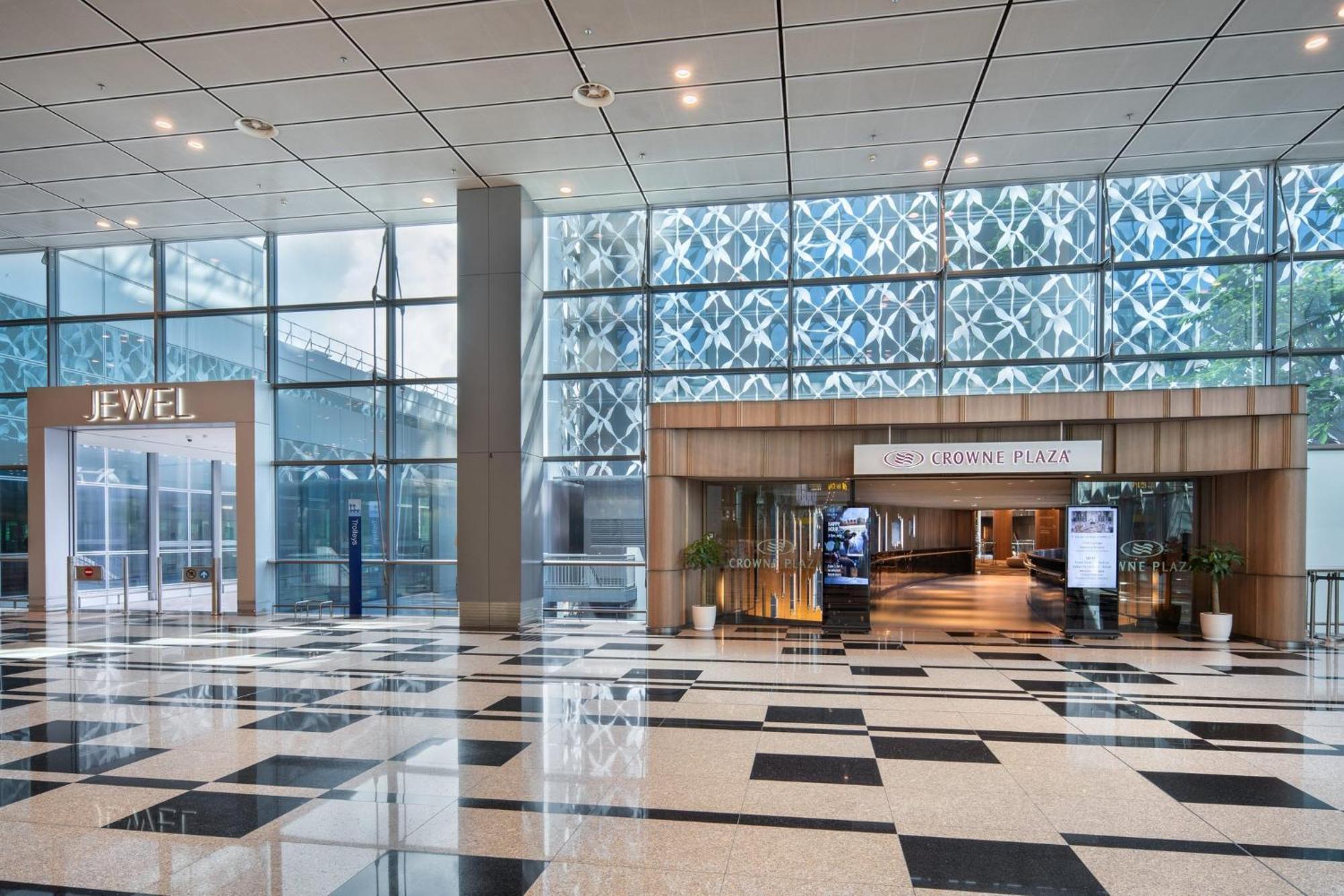 Crowne Plaza Changi Airport By Ihg Σιγκαπούρη Εξωτερικό φωτογραφία The photo shows an indoor area with a modern architectural design featuring large glass windows that allow natural light to enter. On the left side, there is a sign for "JEWEL," indicating a retail or entertainment space. In the center, there is a wo