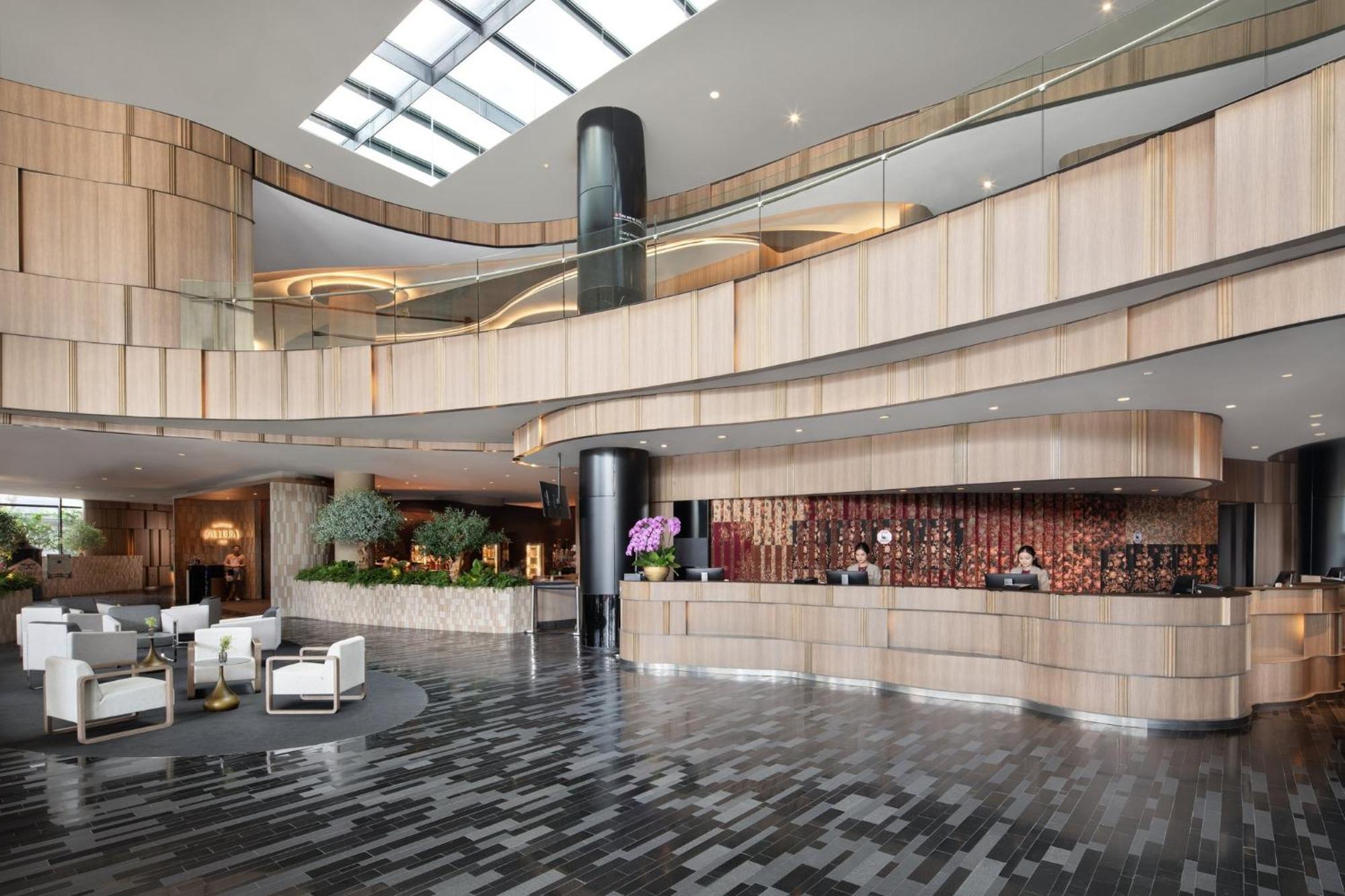 Crowne Plaza Changi Airport By Ihg Σιγκαπούρη Εξωτερικό φωτογραφία The photo shows a modern hotel lobby with a sleek and stylish design. The reception area features a curved wooden counter, with staff members attending to guests. The interior design includes a mix of wood and stone materials, creating a warm and inv