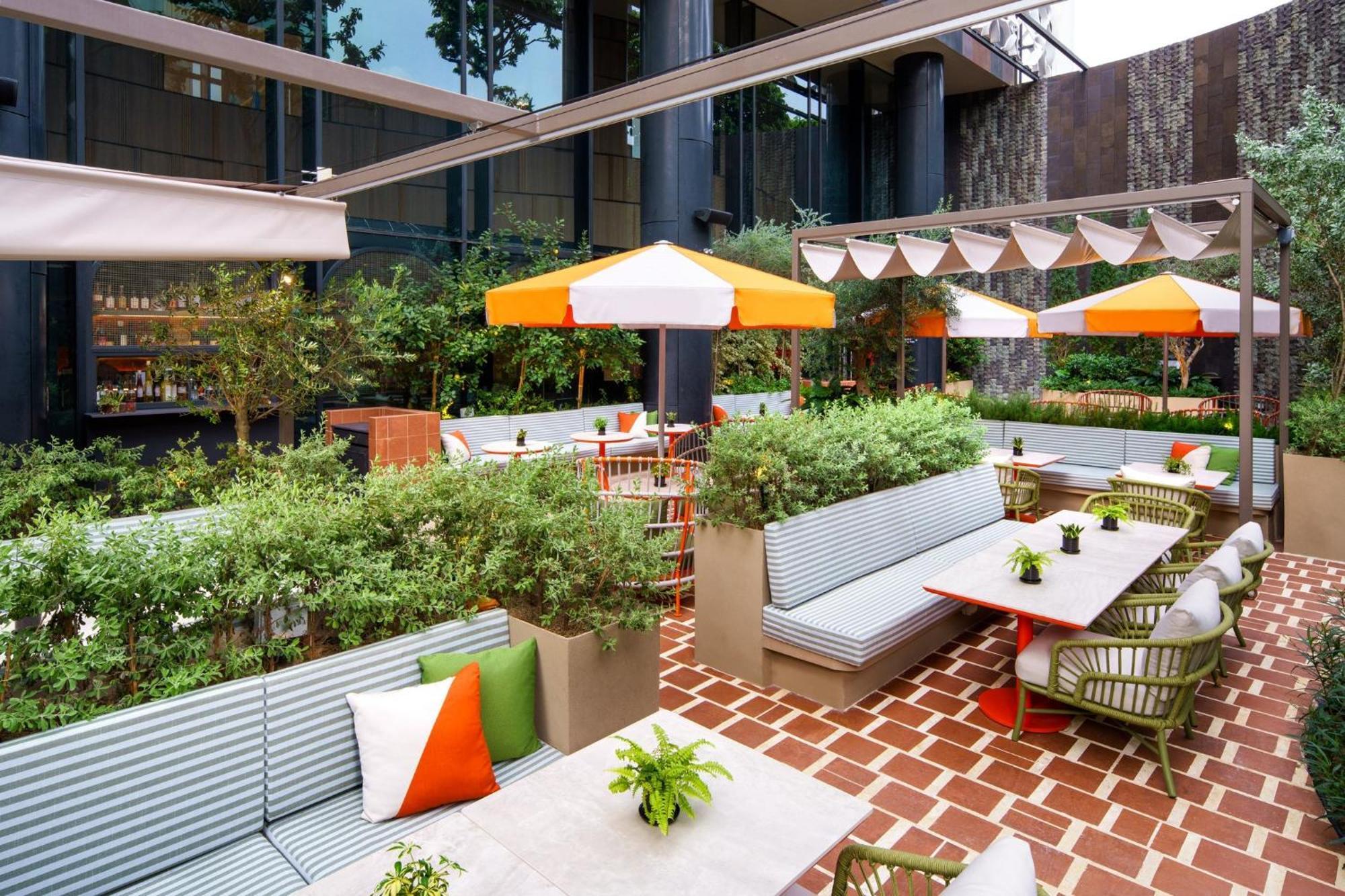 Crowne Plaza Changi Airport By Ihg Σιγκαπούρη Εξωτερικό φωτογραφία The photo depicts a stylish outdoor seating area in a modern setting. It features several light gray benches with colorful cushions, arranged around tables. The space is adorned with green plants and small potted flowers, adding a touch of nature. Th